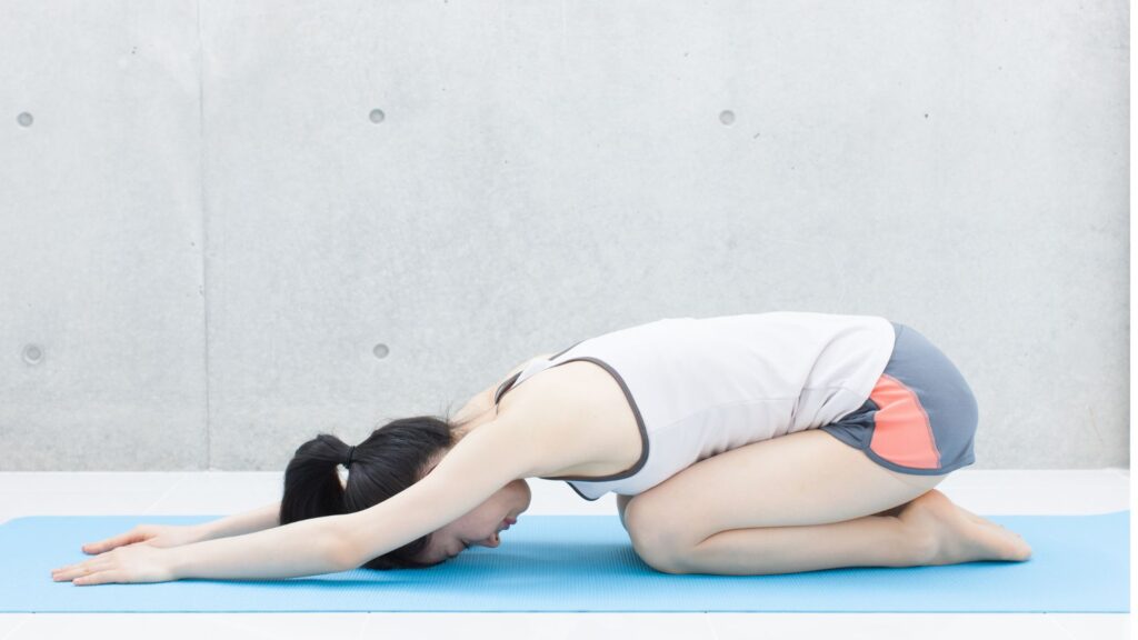 青いマットの上で正座から上体を前に倒し、おでこを床につけて休むポーズ