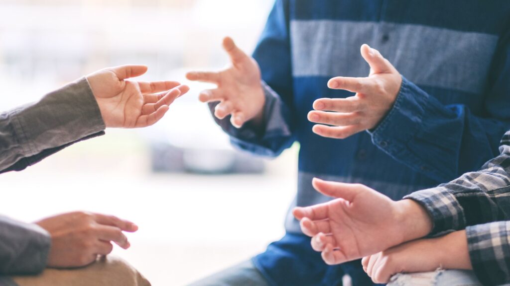 輪になって座り、身振り手振りを交えて対話や相談をしている複数の人の手元